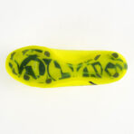 Bottom view of a neon yellow soccer cleat, showing its studded sole with dark green/black studs against a white background