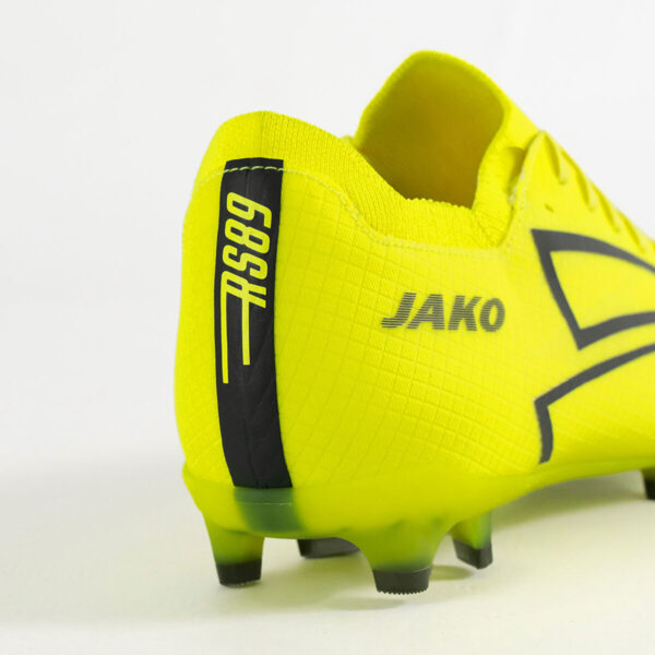 5550_676_P08 Close-up of a neon yellow Jako soccer cleat showing a textured surface and black heel pull tab.