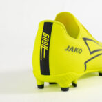 Bright yellow Jako soccer cleat viewed from the heel, featuring a black vertical stripe and studded sole on a white background.