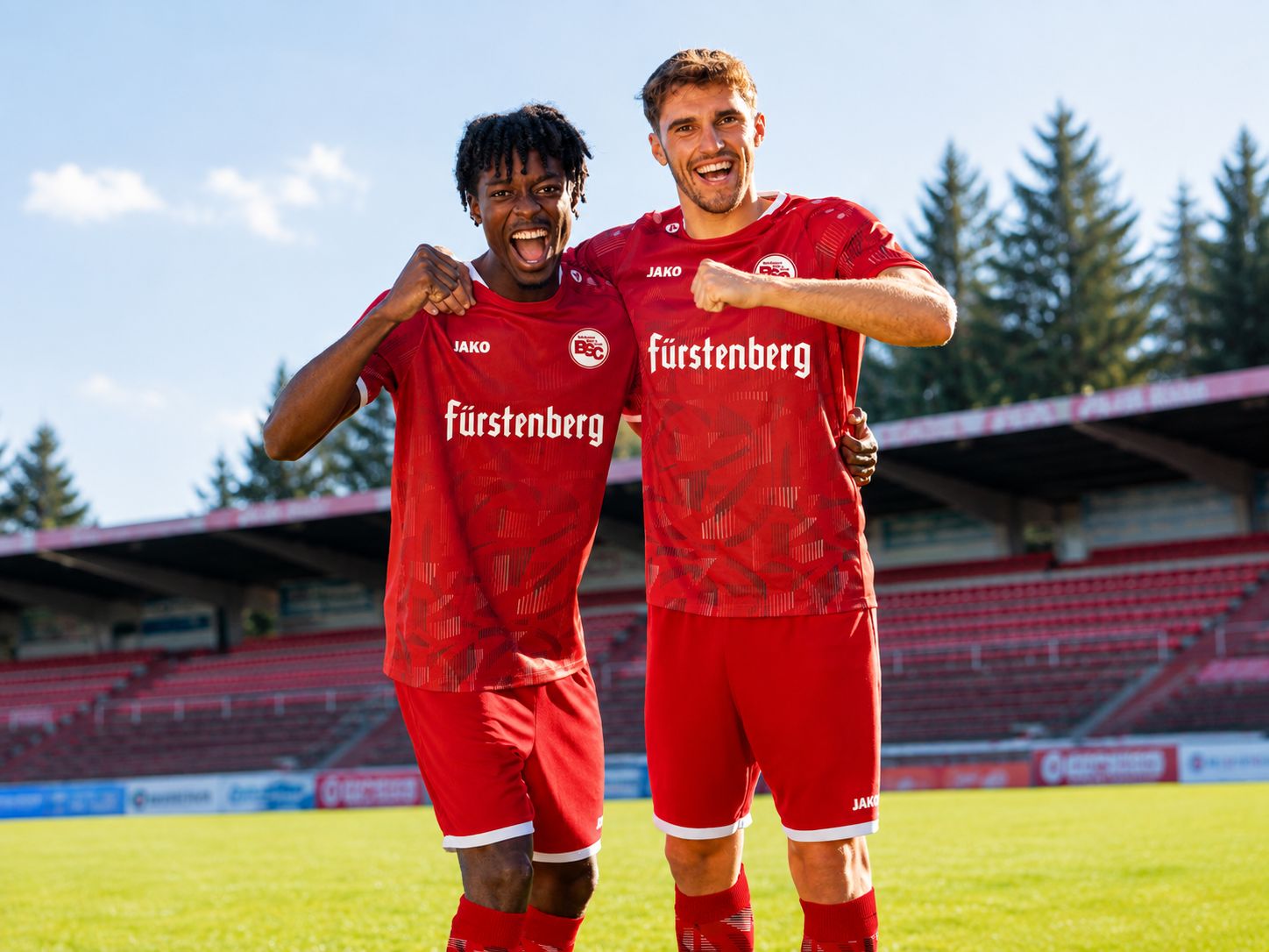 Twee voetballers in rode shirts vieren samen feest op een zonnig voetbalveld